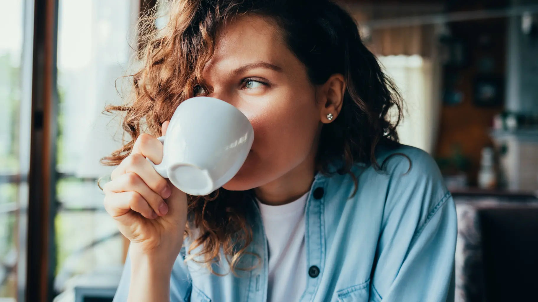 Žena pije kávu v obývacím pokoji, ilustrující vliv jídla a nápojů na skvrny na zubech v článku o ústní hygieně.