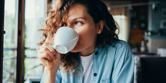 Žena pije kávu v obývacím pokoji, ilustrující vliv jídla a nápojů na skvrny na zubech v článku o ústní hygieně.